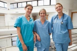 Three smiling nurses leaning against railing at hospital stairwell
